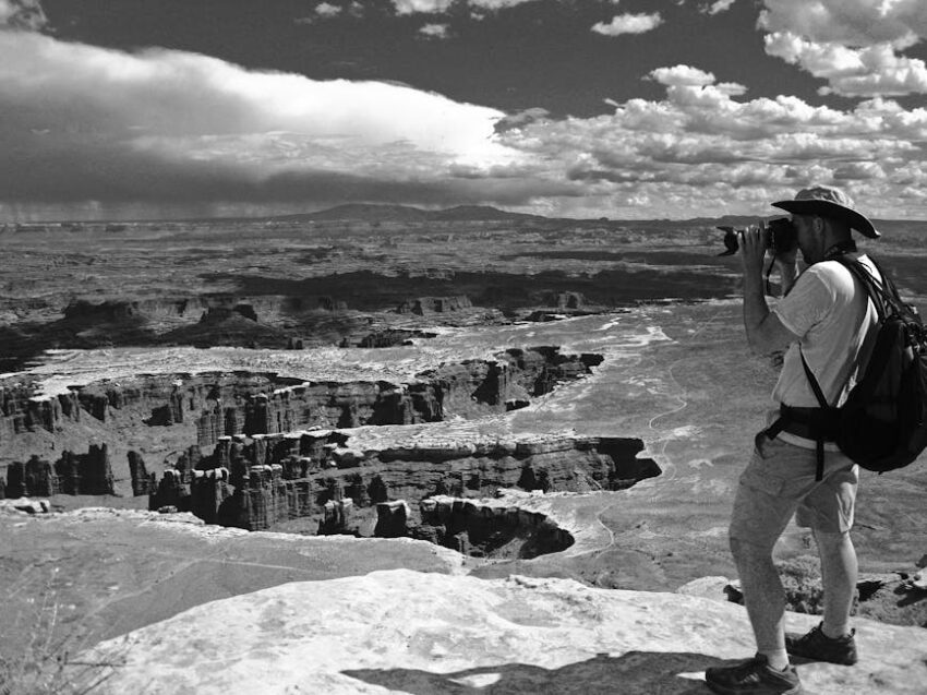 Grayscale Photo of Man Taking Photo of Canyons